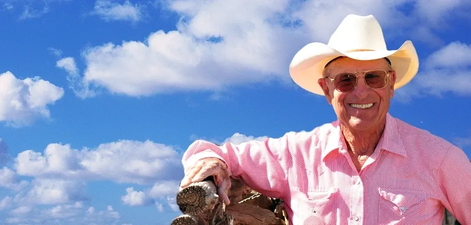 A man in pink shirt and cowboy hat holding something.